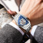 Alcom Distribution men's triangle case wristwatch with silver band and blue skeleton dial on wrist