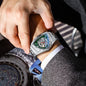 Alcom Distribution men's triangle case wristwatch with silver metal band and green skeleton dial on wrist