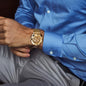 Forsining skeleton watch with gold metal band worn on wrist of man in blue shirt and gray pants