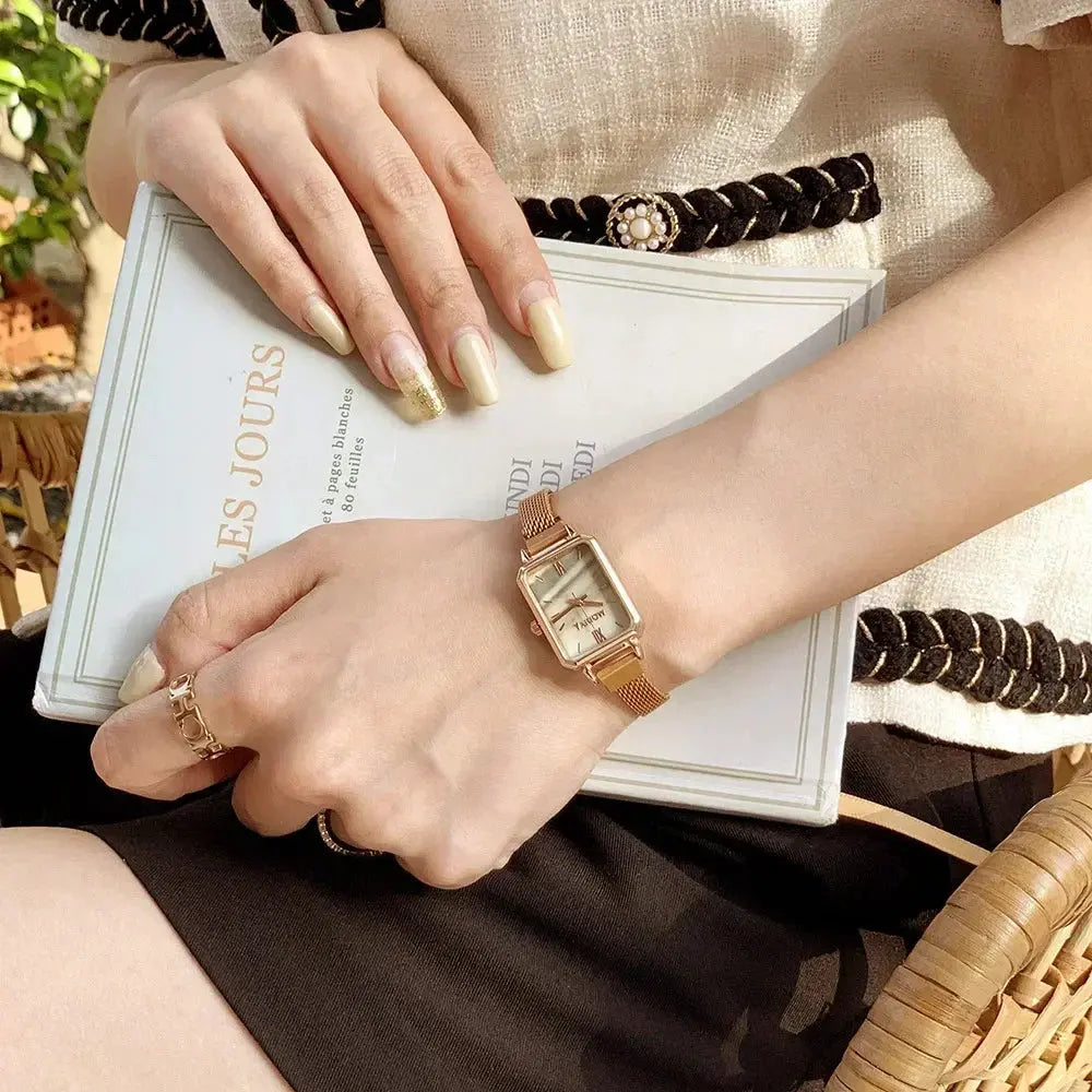 Alcom Distribution rose gold fashion ladies watch rectangular dial mesh band on a styled wrist holding a book