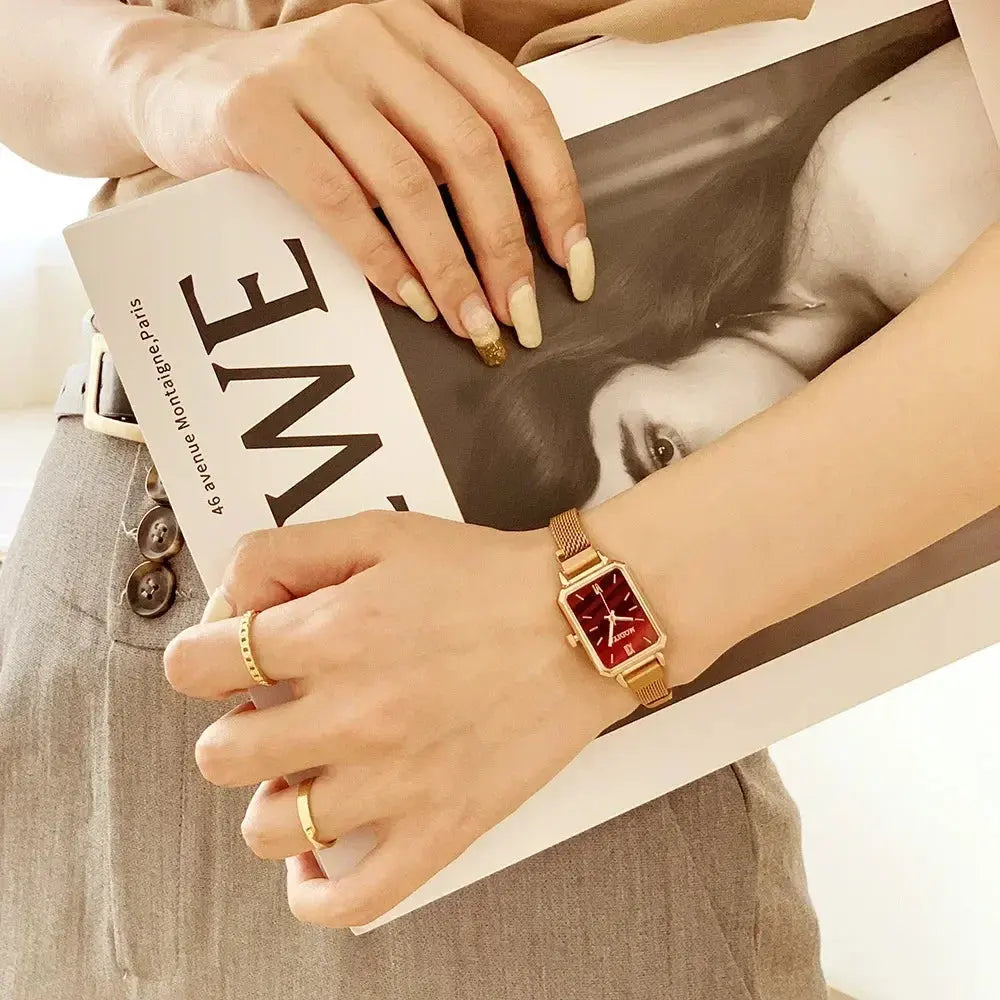Alcom Distribution rose gold fashion ladies watch with rectangular red dial and mesh strap styled on wrist holding magazine
