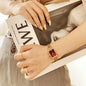 Alcom Distribution rose gold fashion ladies watch with rectangular red dial and mesh strap styled on wrist holding magazine