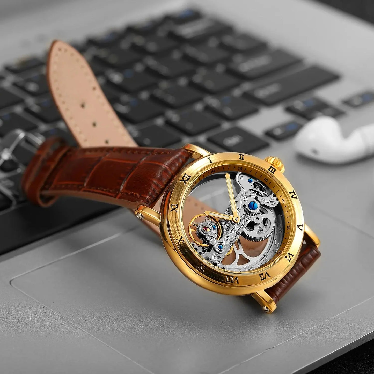 Vintage golden skeleton watch with brown leather strap placed on a laptop keyboard