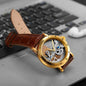 Vintage golden skeleton watch with brown leather strap placed on a laptop keyboard