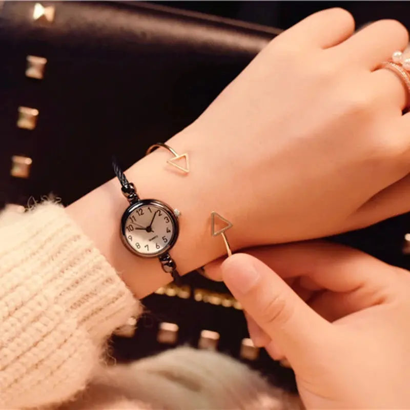 Retro gold bangle watch with a black leather strap worn on wrist with gold triangle accents