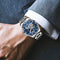 Glenaw rotating earth watch with blue dial and silver metal band on wrist in formal attire