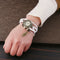 Shourui quartz wristwatch for women with white braided strap and antique bronze charm by Alcom Distribution